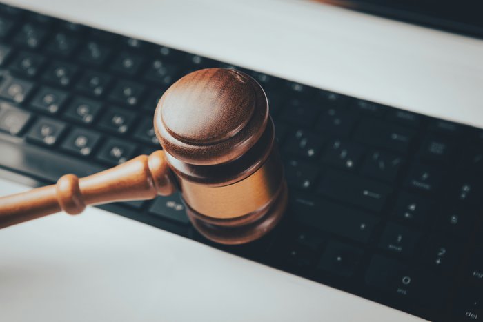 Ein Holzgavel (Richterhammer) liegt schräg auf der schwarzen Tastatur eines Laptops.