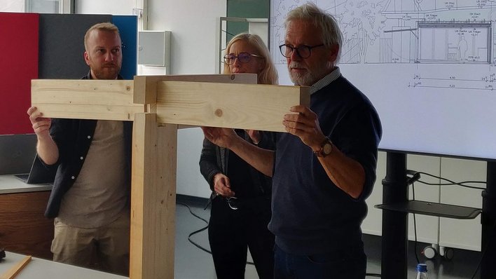 Drei Personen halten die Holzbalken eines Knotenpunkts