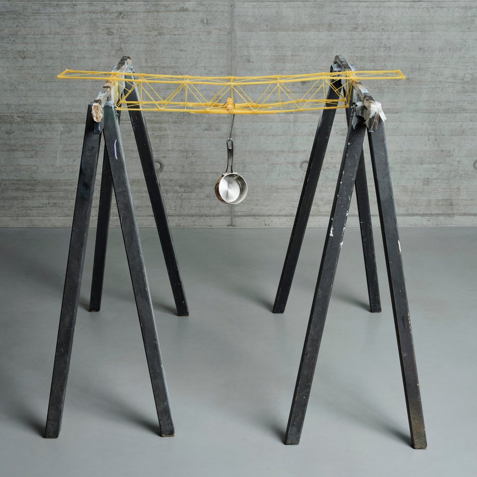 Darstellung einer Brücke aus Spaghetti, an der eine Pfanne hängt