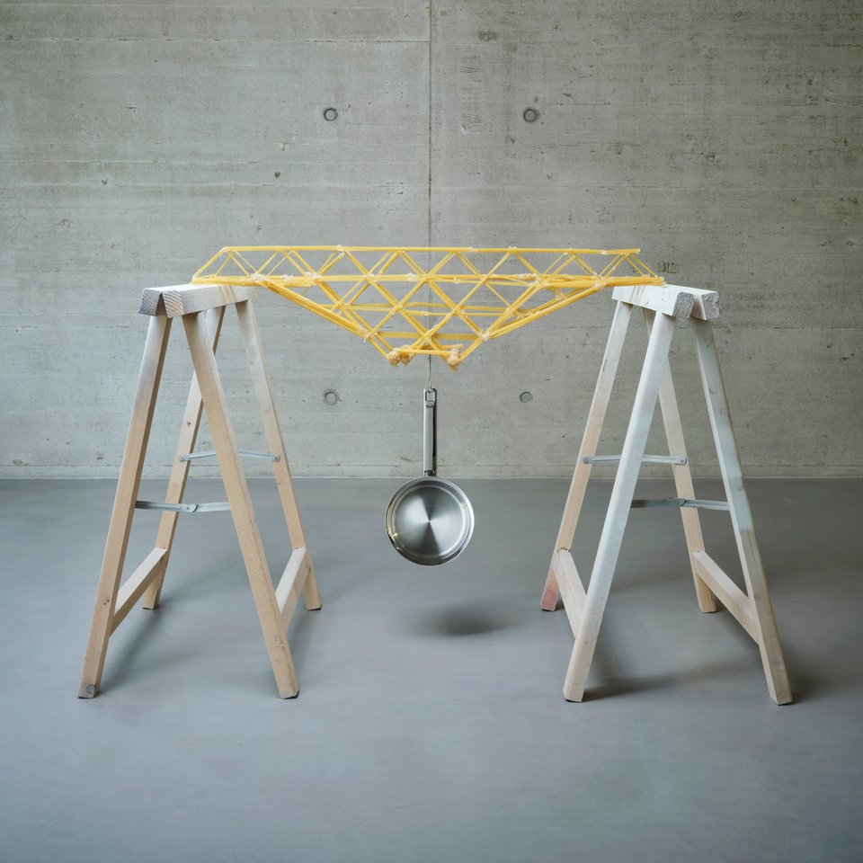 Darstellung einer Brücke aus Spaghetti, an der eine Pfanne hängt