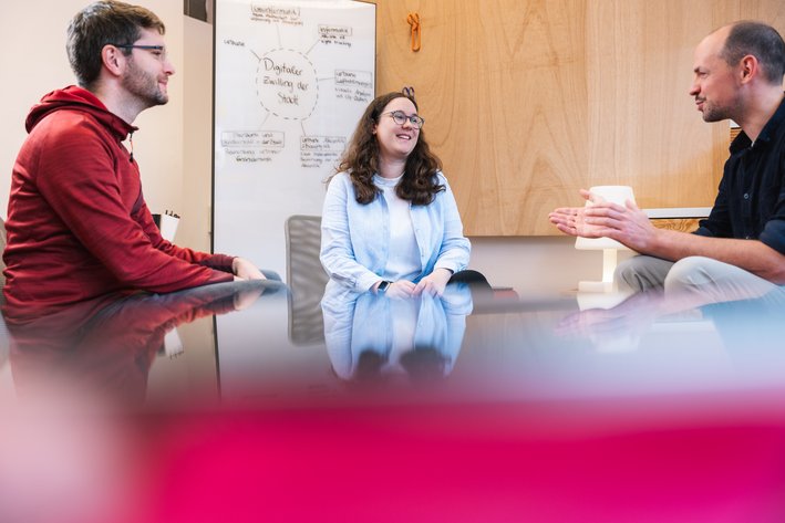 eine weibliche Person und zwei männliche Personen sitzen zusammen und unterhalten sich