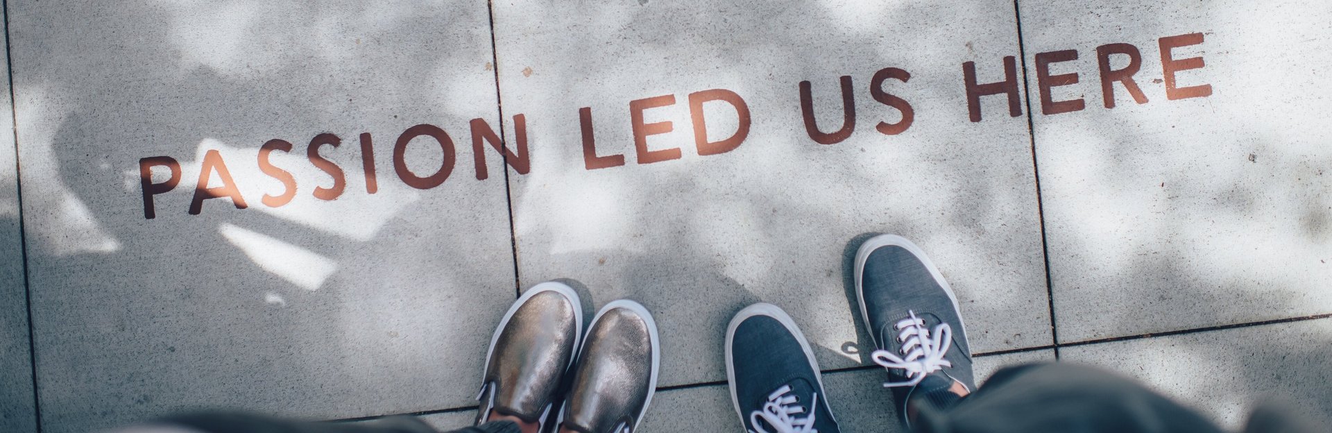 Zwei Menschen stehen auf dem Gehsteig vor einem Schriftzug, der lautet "Passion led us here".