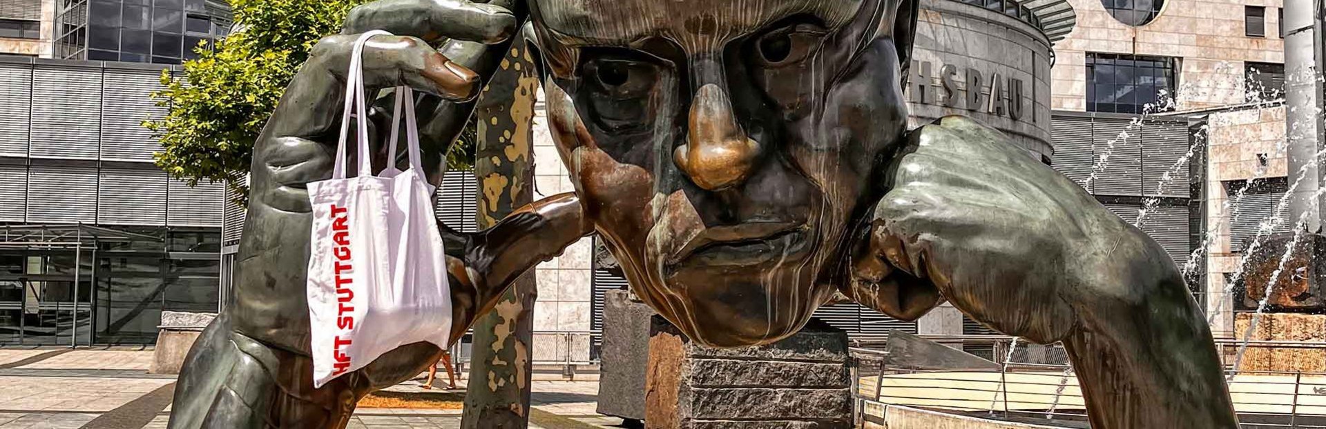 Die Statue "Der Denker" in Stuttgart mit einem HFT Stuttgart Jute-Beutel an der Hand