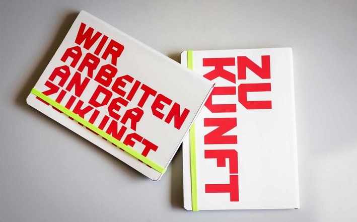 Notizbücher aus weißem Recycling-Leder mit roter Aufschrift "Wir arbeiten an der Zukunft" und "Zukunft".