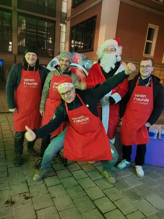 6 Mitglieder des Vorstands und der Beisitzer des Vereins Freunde posieren in roten gebrandeten Schürzen für ein Bild auf der Weihnachtsfeier
