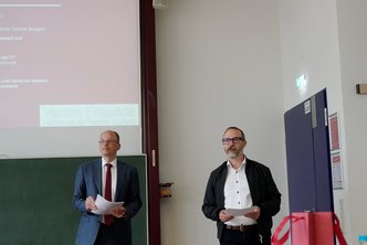 2 Männer halten eine Rede und überreichen einen Preis