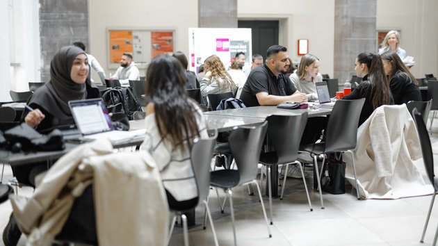 Studierende sitzen an Tischen. Sie lernen und diskutieren miteinander.