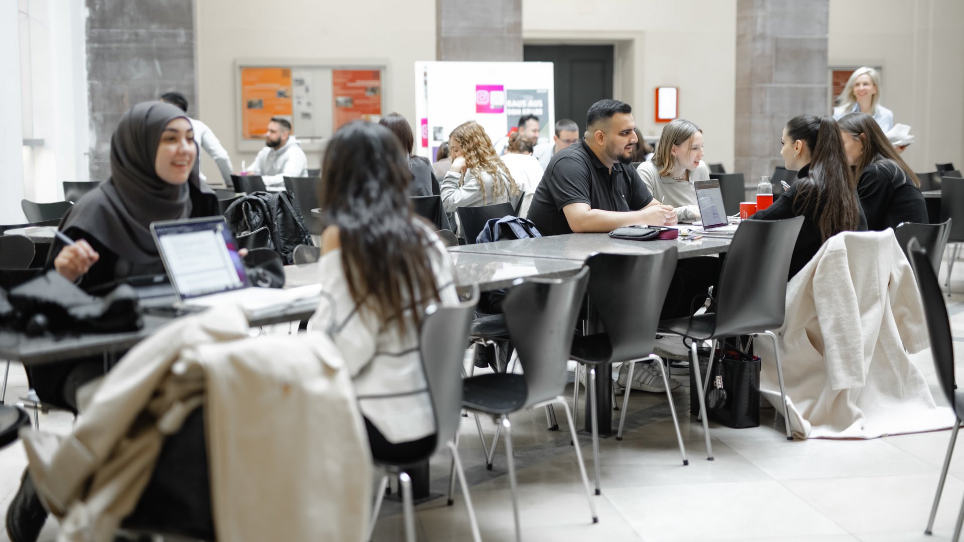 Studierende sitzen an Tischen. Sie lernen und diskutieren miteinander.
