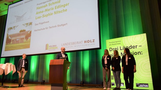 Drei Studentinnen stehen auf der Bühne und werden mit einem Preis ausgezeichnet.