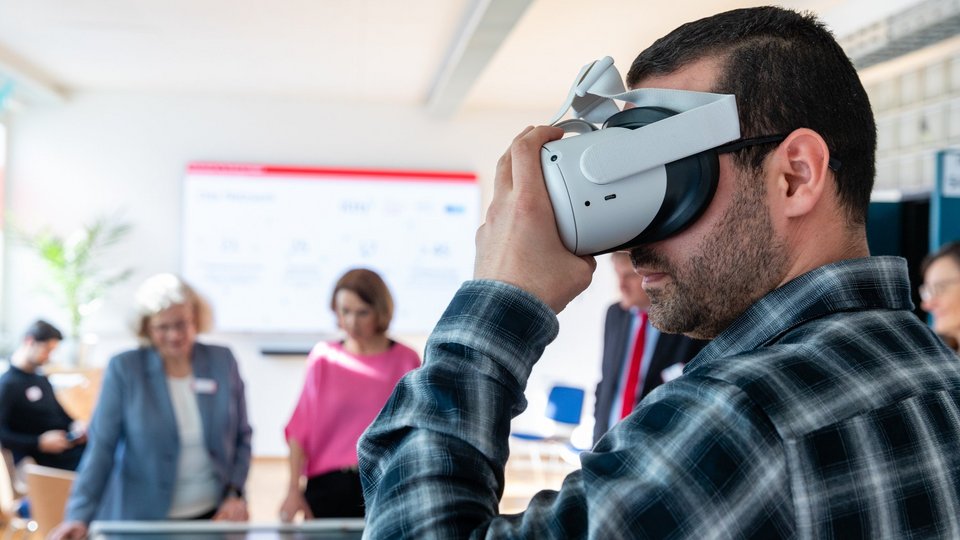 Ein Mitarbeiter präsentiert Petra Olschowski eine VR-Brille