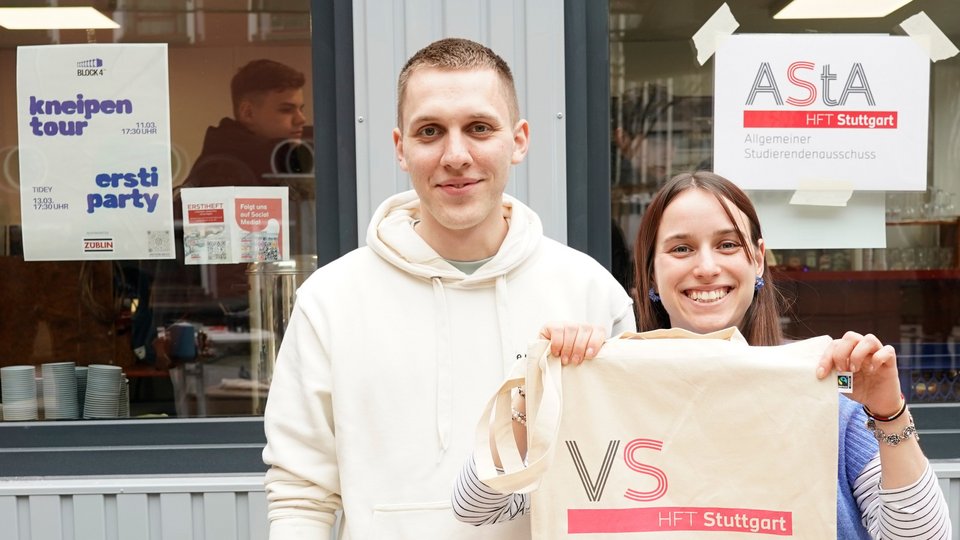 Zwei Studierende zeigen Merchandise-Artikel der Hochschule.