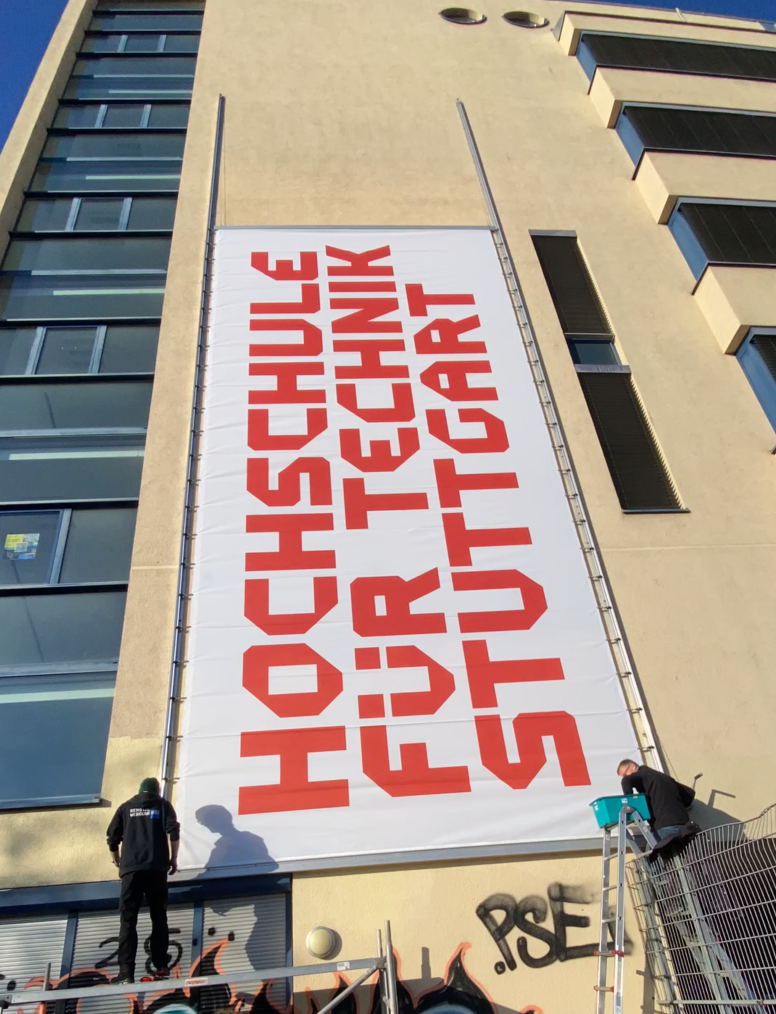 HFT Banner wird an die Fassade des neuen Gebäudes der SBS angebracht